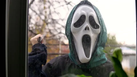 An unknown person appears outside the window in a screaming mask with a knife in Stock Footage 163779039