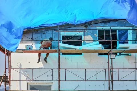 Unknown worker sitting on a scaffolding, installing foamboard thermal insul.. Stock Photos