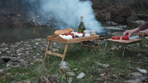 Unknown young woman using kitchen knife cutting fresh tomato near campfire Stock Footage 271546352