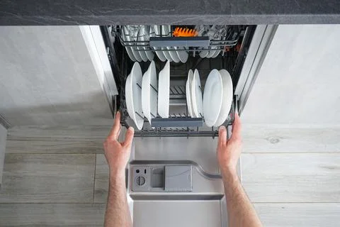Unloading the dishwasher, man's hands. Dishwasher flat lay. Stock Photos