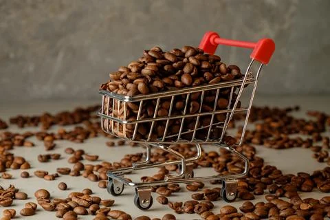 Unloading roasted coffee beans in a mini shopping cart on a light surface Stock Photos