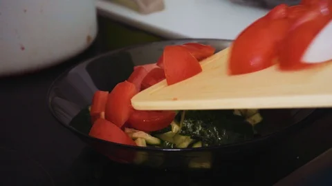 Unloading sliced tomatoes from a cutting board into a plate of clear dark glass Stock Footage 112043560