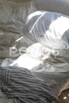 Unmade bed with messy duvet cover in morning light Stock Photos