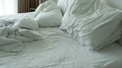 Unmade bed with rumpled white sheets and pillows, showcasing the gradual 스톡 동영상 330165325