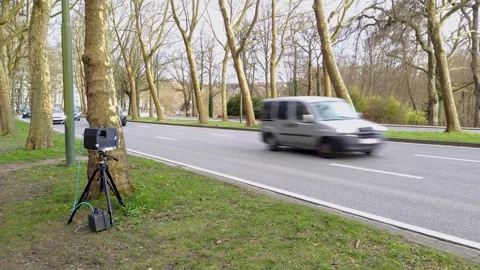 Unmanned speed camera positioned behind a tree monitoring vehicles and 스톡 동영상 331415239
