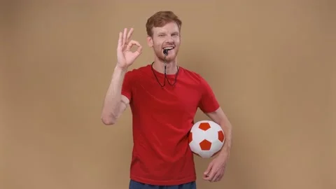 Unny man on a beige studio background coach with a ball and a whistle shows an Stock Footage 200876985