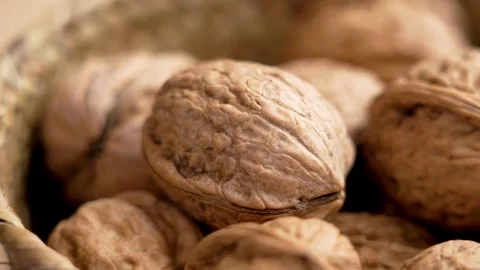 Unpeeled whole walnut with nut shells falling into a rustic bowl Stock Footage 279478664