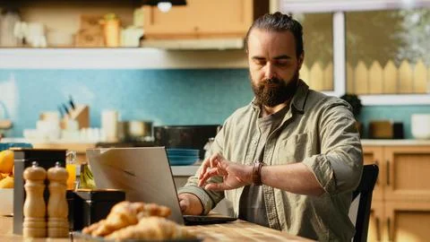 Unpunctual man, checking time on wrist watch, wooden kitchen table Stock Photos