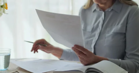 Unrecognisable elderly lady looking through utility bills and typing on laptop. 库存影片 334061754