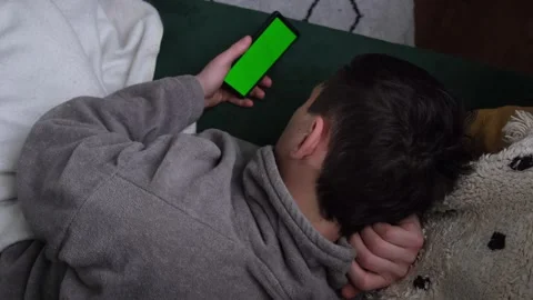 Unrecognised man on a sofa in a robe is watching a phone with a green chroma key Stock Footage 312973755