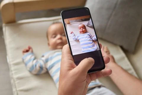 Unrecognizable anonymous man sitting on sofa with his infant son capturing .. Stock Photos