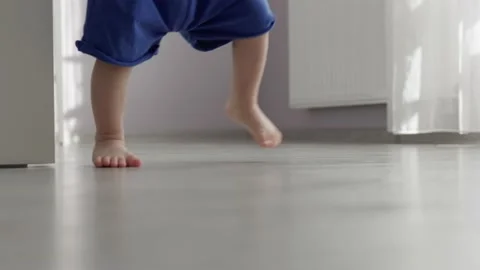 Unrecognizable baby toddler doing first steps barefoot, grey floor room indoors Stock Footage 171615519