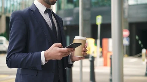 Unrecognizable bearded businessman drinking coffee, using phone in street Stock Footage 95591453