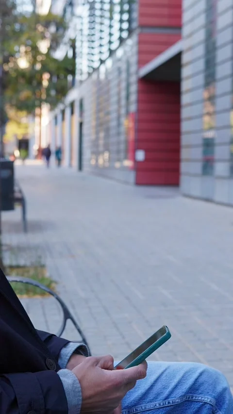 Unrecognizable businessman using smartphone while seated on bench outdoors Stock Footage 345247411
