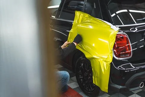 Unrecognizable car wrapper in black protective gloves using a squeegee to Stock Photos