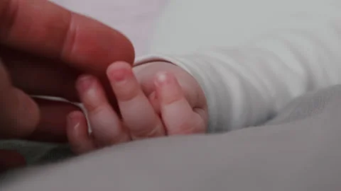 Unrecognizable caring young father holds and touches baby hand lying on bed Stock-Footage 150426499