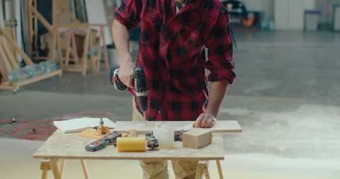 Unrecognizable carpenter using an electric drill to install a screw on a wooden Stock Footage 199618637
