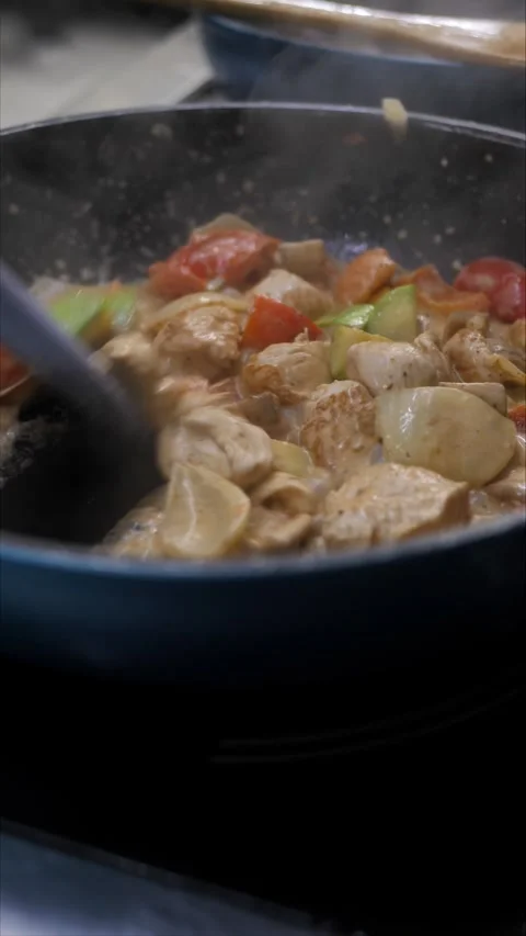 Unrecognizable chef frying vegetables and meat on a hot frying pan while cooking Stock Footage 306323472