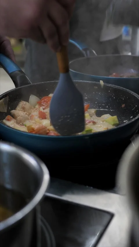 Unrecognizable chef frying vegetables and meat on a hot frying pan while cooking Stock Footage 306747119