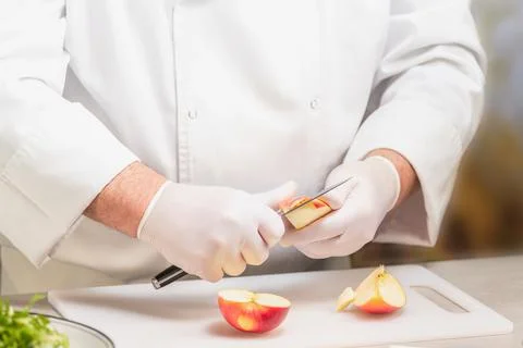 Unrecognizable chef in uniform cutting an apple on a plastic cutting board Stock Photos
