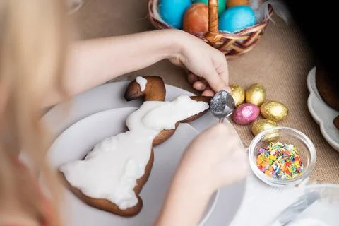 Unrecognizable child topping Easter bunny shaped cookie with icing on festive Stock Photos