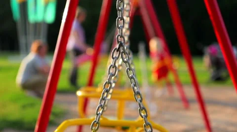 Unrecognizable children ride on the swings at the playground Stock Footage