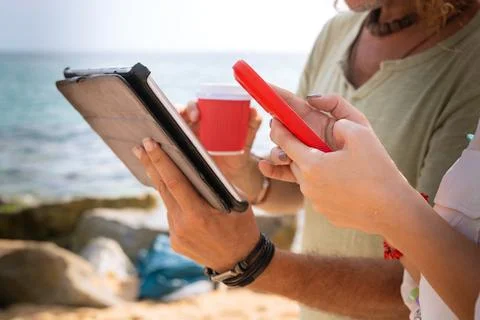 Unrecognizable couple on the beach browsing digital tablet and smartphone apps. Stock Photos