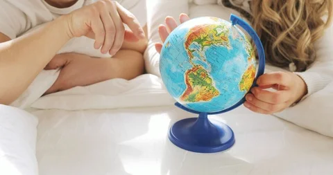 Unrecognizable couple in bed are looking at globe spinning it and pointing at Stock Footage 105489487