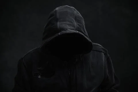 Unrecognizable cyber criminal or computer hacker wearing black hooded jacke.. Stock Photos