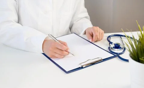 Unrecognizable doctor wrtining down notes in history of disease with stethosc Stock Photos