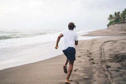 Unrecognizable ethnic man running on empty seashore Stock Photos