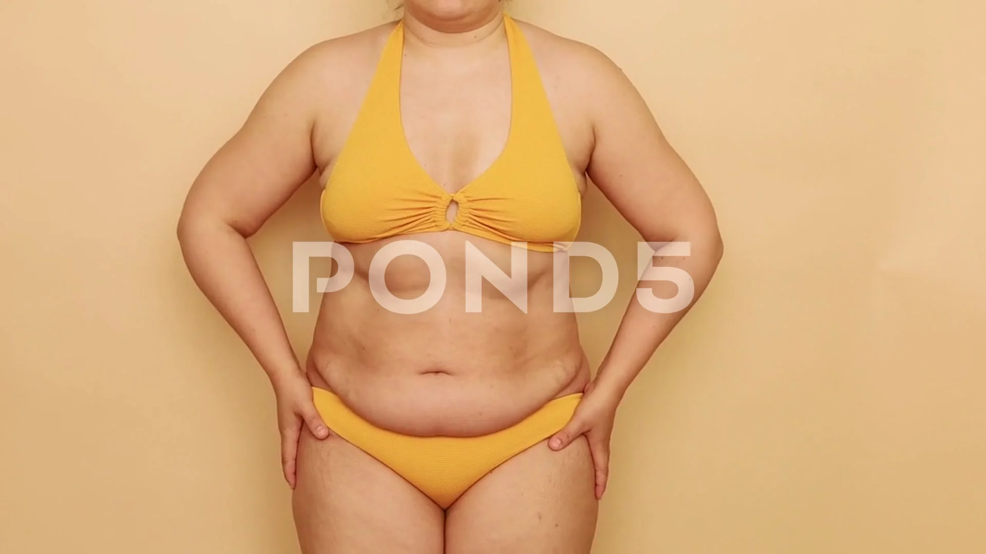 Unrecognizable fat plump woman wearing yellow bra bikini sucking in excess fat