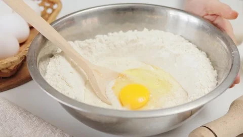 Unrecognizable female baker adding eggs to the dough stirring gently prepares Stockbeeldmateriaal 293282222