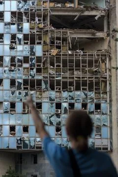 Unrecognizable girl back to camera points at building destroyed by war drones Stock Photos