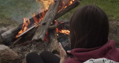 Unrecognizable Girl Sitting By The Fire Using Smartphone Close-up. Faceless Stock Footage 139873286