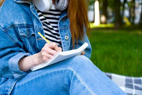 Unrecognizable girl takes down notes in notebook in the park.Distant learning Stock Photos