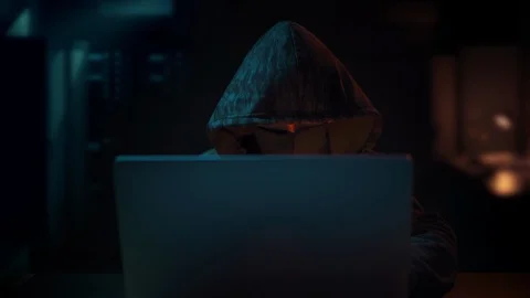 Unrecognizable Hacker with hooded face and mask coding on computer late night Stock Footage 129392142