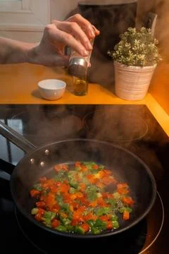 Unrecognizable hand throwing salt and cooking vegetables in a frying pan Stock Photos
