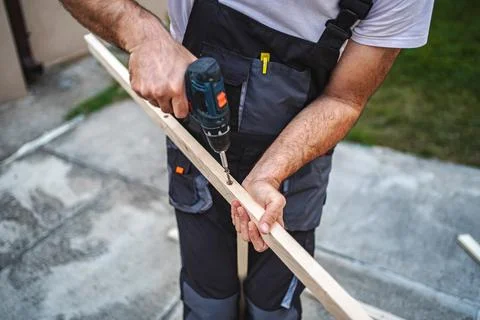 Unrecognizable male carpenter using electric screwdriver on a wooden plank Stock Photos