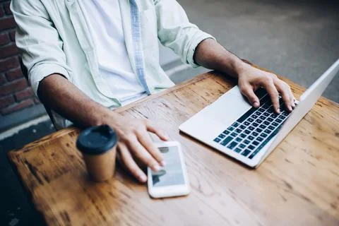 Unrecognizable male remote worker using netbook and cellphone in street Stock Photos