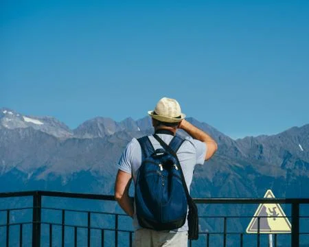 Unrecognizable man with backpack standing on observation deck in mountains bl Stock Photos
