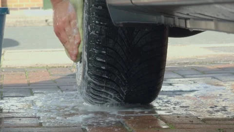 Unrecognizable man cleaning car wheel with sponge at home driveway, saving money Stock Footage 333246981