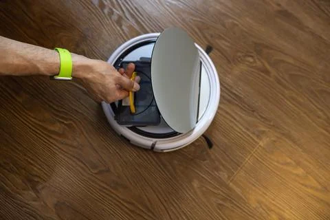 Unrecognizable man cleans a robot vacuum cleaner. Takes out or inserts the du Stock Photos