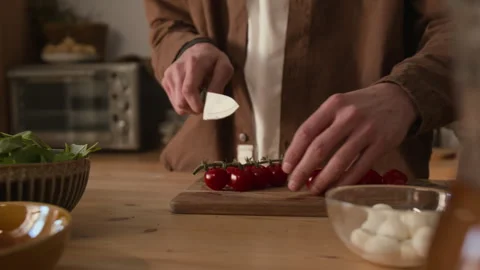 Unrecognizable Man Cutting Cherry Tomato in Half on Wooden Cutting Board Stock Footage 303046809