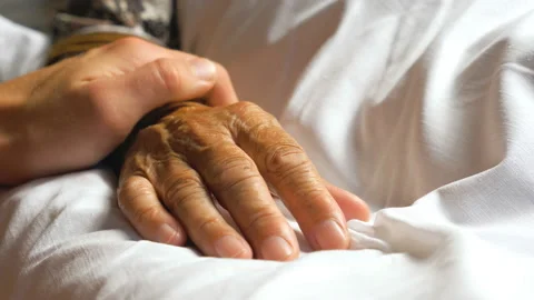 Unrecognizable man gently stroking hand of his sick mother showing care or love Stock Footage 124555331