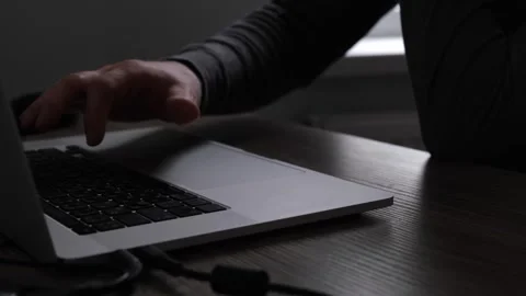 An unrecognizable man in gray sits at a table, uses a laptop in the dark and Stock Footage 274633268