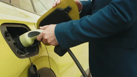 Unrecognizable man inserts power connector into EV car. Male hand plugging in Stock Footage 235230585