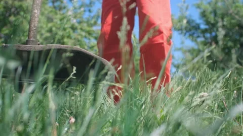 An unrecognizable man in an orange boilersuit is cutting grass with a motor trim Vídeos de archivo 194734069
