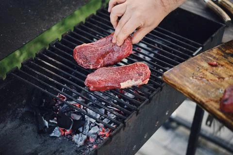 Unrecognizable man put raw strip steaks on hot grill Stock-Fotos