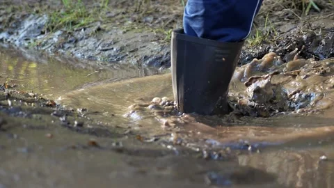 Unrecognizable man in rubber boots steps into a muddy puddle, water splash, slow Stock Footage 154910798